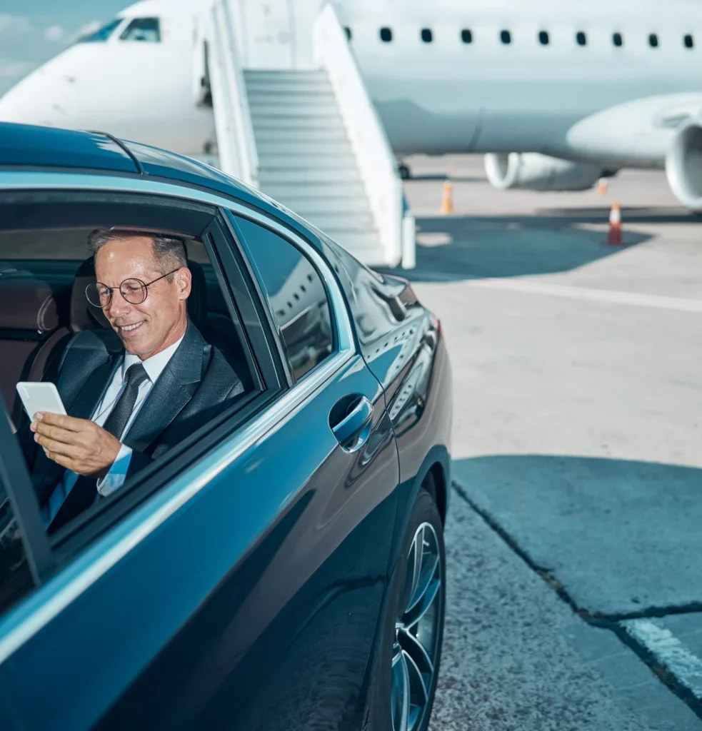 A suited businessman seated in a car, using his phone, looking focused and professional.