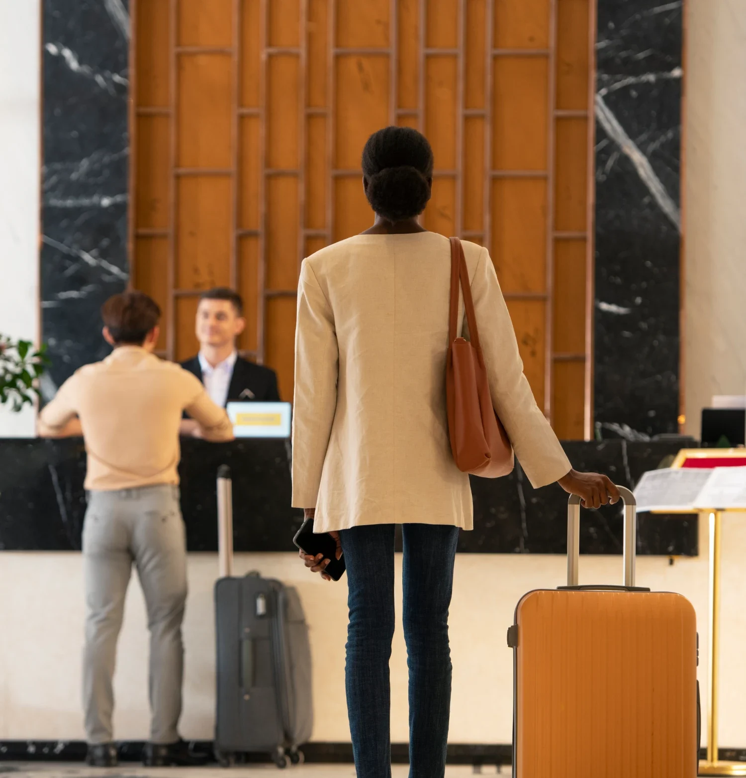 A woman with a suitcase stands outside a hotel, preparing for her stay or departure.